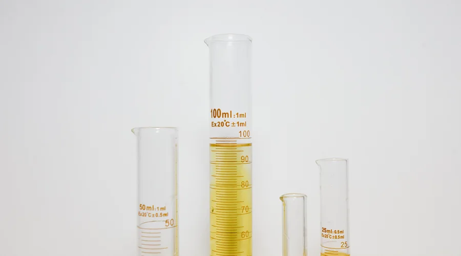 2-stroke premix oil ratio — measured two-stroke oil swirling into gasoline inside a graduated glass mixing vessel on a workshop bench | Global Formulation